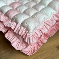 a pink and white bed with ruffles on the bottom layer is laying on a wooden floor