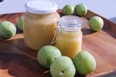 some green apples are on a wooden tray with a glass jar and some other fruit