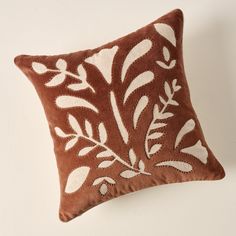 a brown and white decorative pillow with leaves on the front, sitting against a wall