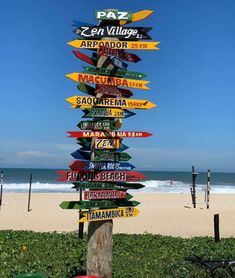 a wooden pole with many different signs on it's side next to the beach