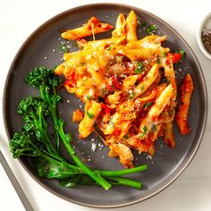 a plate with pasta and broccoli on it next to a bowl of seasoning