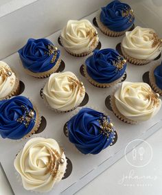 twelve blue and white cupcakes in a box with frosting on top, decorated with gold sprinkles