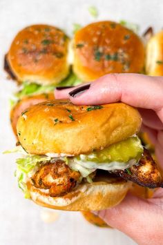 a hand holding a sandwich with shrimp and lettuce on it in front of other burgers