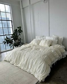 an unmade bed sitting in front of a window next to a potted plant