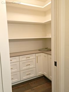 an empty kitchen with white cupboards and counters in the corner, looking into the pantry