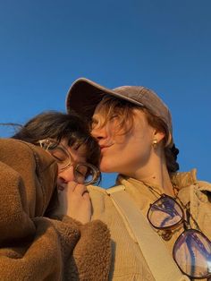 two women are kissing each other while wearing hats and glasses on a sunny day with blue skies in the background