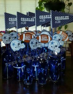 a table topped with blue vases filled with football themed cups and paper flags on top of them