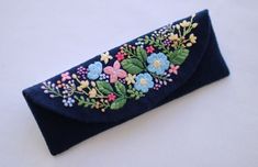 a blue case with flowers and leaves embroidered on the side, sitting on a white surface