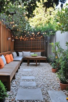 Cozy outdoor patio with string lights, wooden seating, orange and gray cushions, potted plants, and a stone pathway. Small Garden Patio Ideas On A Budget, Patio On Side Of House, Small Patio Pavers Design, Painted Patio Ideas, Small Deck Inspiration, Small Patio Oasis Ideas, Small Patio Design On A Budget, Small Wood Patio, Small Backyard Patio Designs Budget