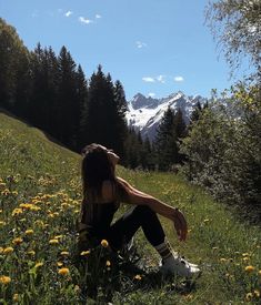 a woman sitting in the grass with mountains in the background