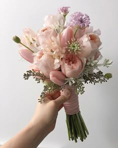 a hand holding a bouquet of pink and white flowers in it's left hand