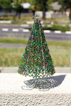 a small christmas tree made out of plastic beads on a cement ledge in front of a street