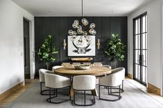 a dining room table surrounded by white chairs and potted plants in front of a black wall