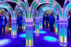 people are standing in the middle of an illuminated tunnel with columns and arches on either side