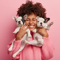 a woman holding three puppies in her arms and smiling at the camera while wearing pink sweater