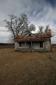 an old run down house sitting in the middle of a field with no leaves on it