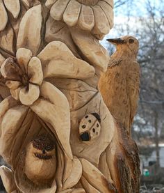 a bird sitting on top of a wooden sculpture next to a tree branch with flowers