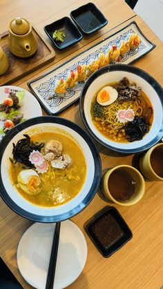 two bowls of soup are sitting on a table with chopsticks and other food