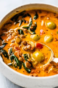 a bowl of soup with olives, spinach and other toppings on top