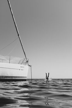 a person on a surfboard in the water next to a sailboat that is upside down