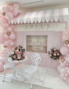 a pink and white room with balloons on the wall, tables and chairs in front of it