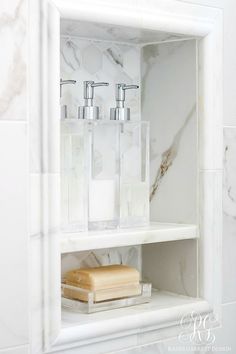 a bathroom shelf with soap and lotion bottles on it in a marble tiled wall