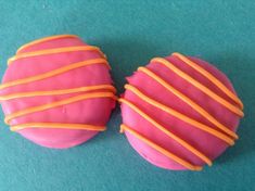 two pink donuts with orange icing on a green surface