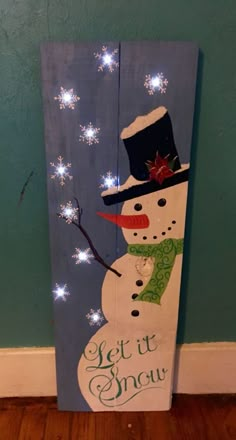 a wooden sign with a snowman wearing a hat and scarf on it that says let it snow