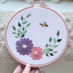 a hand holding a pink and purple flower with a bee on it's back