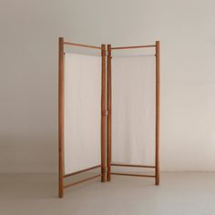 a room divider made out of wood and white fabric on the top, in front of a plain wall