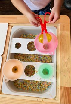 a child is playing with sprinkles and scissors in a tray on the table