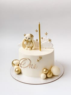 a white cake with gold decorations and a teddy bear on top