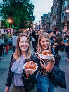 two young women holding plates of food in their hands while walking down the street at night