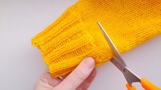 someone using scissors to cut the edge of a knitted yellow cloth