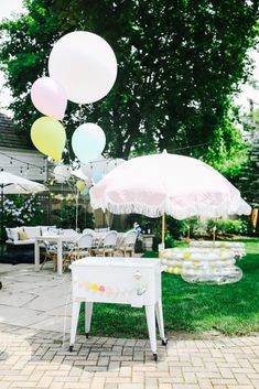 an outdoor party with balloons and umbrellas in the grass, on a brick patio