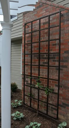 a brick building with a white pergolated trellis next to it and plants growing in the ground