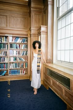 a woman standing in front of a bookshelf holding a skateboard