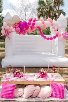 a table topped with pink and white balloons next to an inflatable bed on top of a field