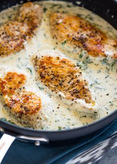 some chicken is cooking in a skillet on the stove with white sauce and parmesan cheese