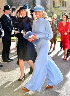 two women in blue dresses and hats walk down the street with other people behind them