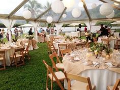 tables and chairs are set up in a tent for an outdoor event with paper lanterns hanging from the ceiling