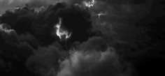 black and white photograph of storm clouds in the sky with an airplane flying above them