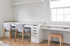 a white desk with two chairs next to it and a window in the back ground