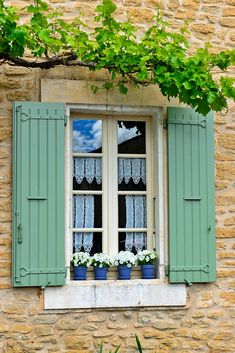 an open window with green shutters and flower pots on the ledge next to it