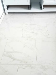 a bathroom with white cabinets and marble flooring