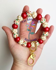 a hand holding a red and white beaded bracelet with a flower charm on it