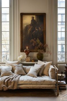 a living room filled with lots of furniture next to two large windows and a painting on the wall