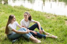 two young women sitting on the grass near water