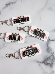 three keychains with the words hawaii, hawaii and kenya printed on them sitting on a marble surface