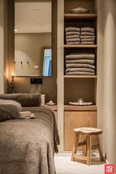 a bed sitting next to a wooden shelf filled with towels